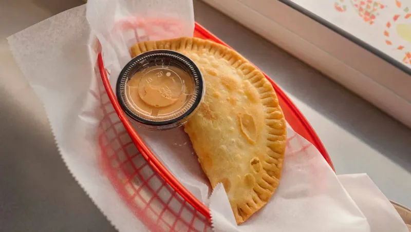 Golden, crimped empanadilla in a red basket with a cup of mayoketchup for dipping